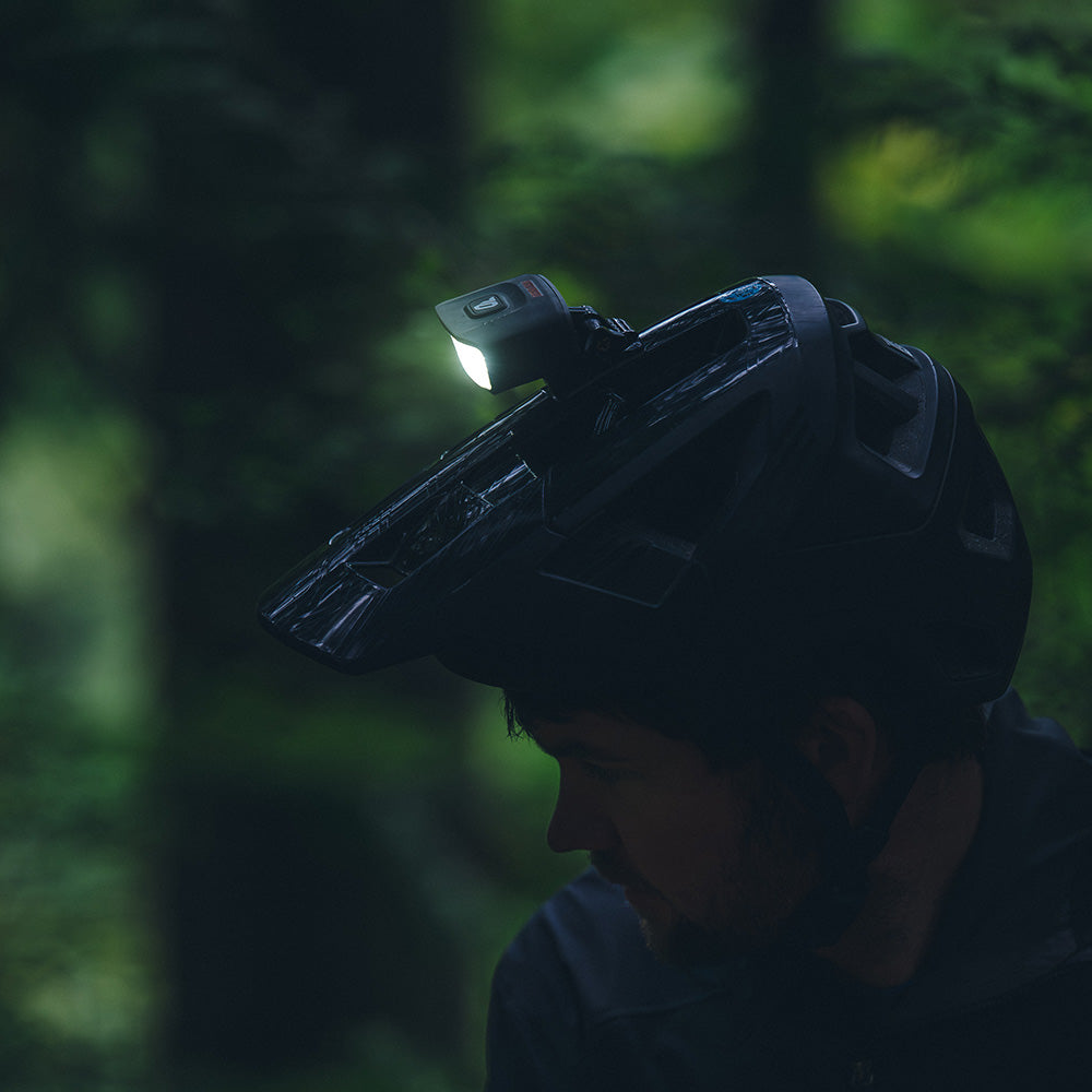 Portal bike helmet light switched on, mounted on a black helmet in a dark forest, side view