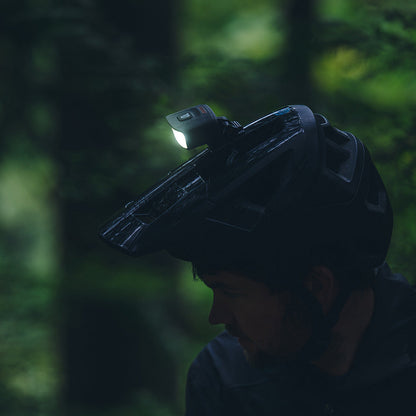 Portal bike helmet light switched on, mounted on a black helmet in a dark forest, side view